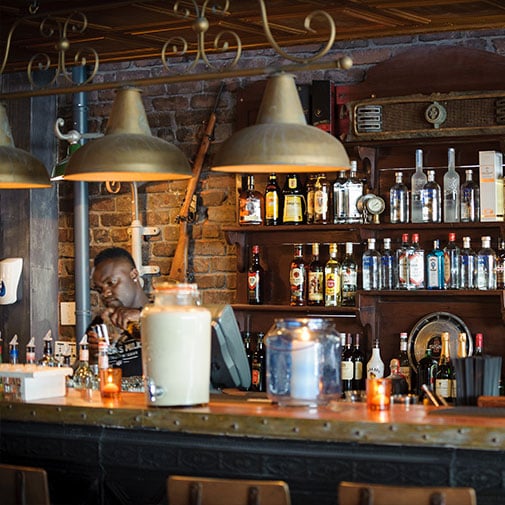 Bottle collection bar with liquor bottles, rustic interior, and warm lighting in a cozy pub setting.