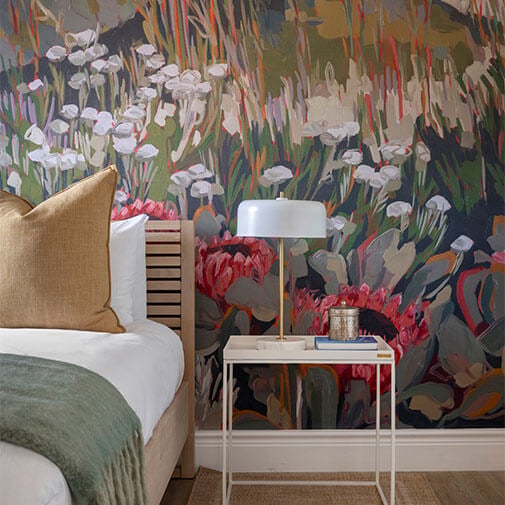 Floral accent wall behind modern bedside table with lamp and books, stylish bedroom decor in South African interior design.