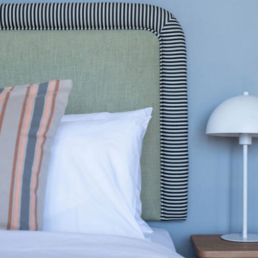 Elegant bedroom with pastel decor, striped cushions, and a modern white bedside lamp for cosy living.