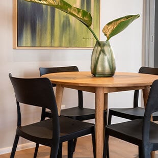 Elegant dining room with wooden table and black chairs featuring a large glass vase with tropical leaves.